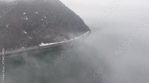 Fly over Lake Inawashiro and descending toward a rare tunnel view through drifting fog and clouds. A serene winter morning scene with calm water and slowly moving mist, ideal for meditation or drive.