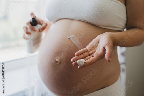 A pregnant woman applies skincare cream to her skin. This moment emphasizes self-care during pregnancy.