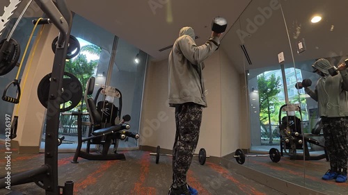 Side view of man performing standing dumbbell curls in a gym