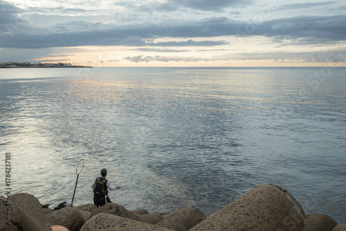a man fishing on the tetrapods beside the evening sea in jeju island