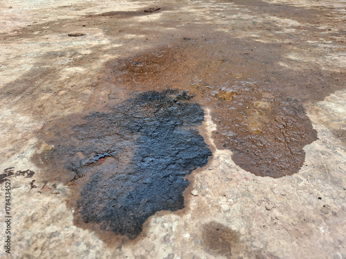 Dark black oil or chemical stain spilled on a rough concrete floor, indicating pollution, hazard, and industrial waste. Liquid spill and messy texture background