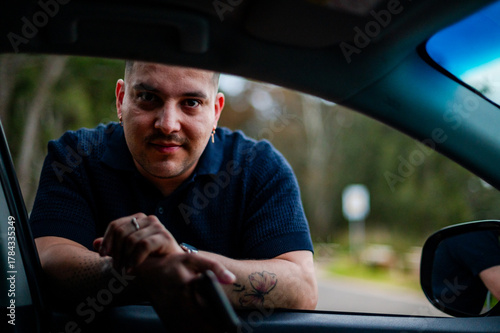 A man leans on a car window form outside vehicle in a park setting