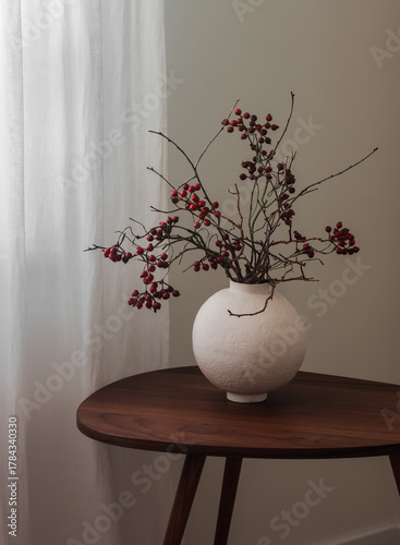 Autumn bouquet of cranberry branches in a round ceramic vase on a wooden table
