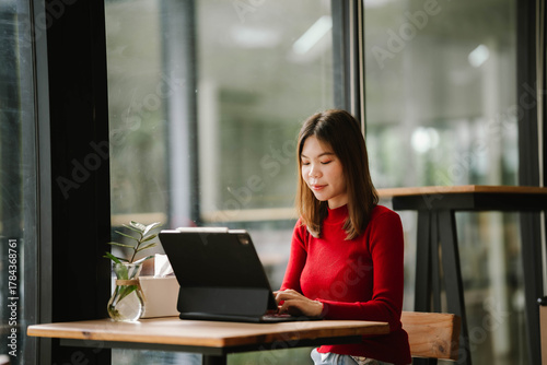 Free Download A woman wearing headphones works on a tablet in a cozy café, focused and relaxed by the window. - GFXLoad