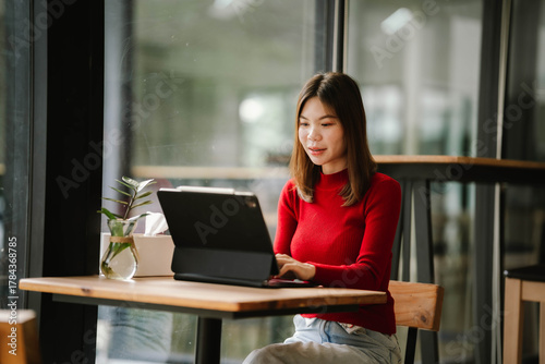 Free Download A woman wearing headphones works on a tablet in a cozy café, focused and relaxed by the window. - GFXLoad