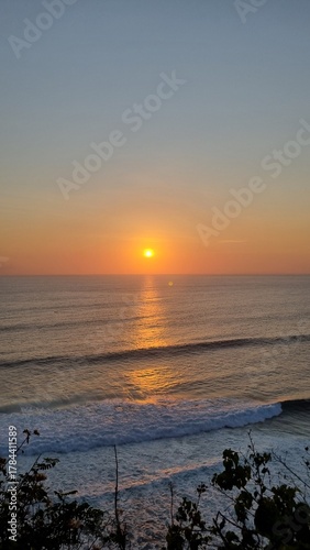 Golden sunset over the ocean viewed from a cliff in Bali, Indonesia. Gentle waves and warm evening light create a calm and romantic atmosphere. Perfect for travel, relaxation and nature themes.