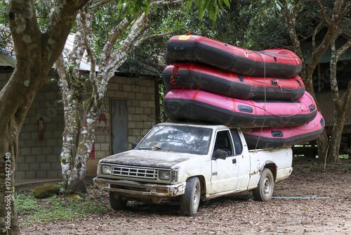 Old white pickup truck transports stack of pink inflatable boat rafts and equipment. This rugged vehicle ready for an adventure, carrying gear through rural jungle