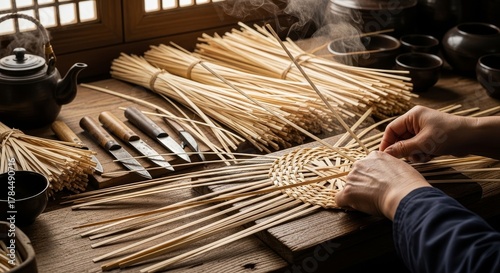 Traditional Japanese artisan hands weaving bamboo strips using specialized carving tools in authentic wooden workshop with steaming teapot background
