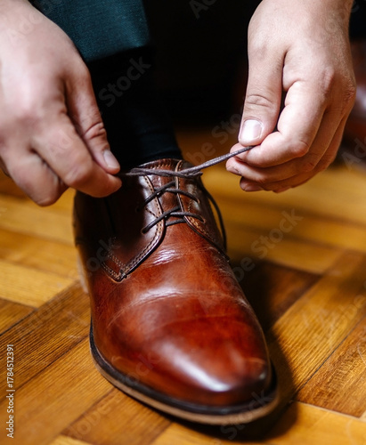 Man is lacing his brown leather shoes