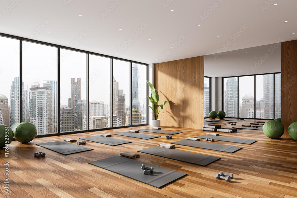 Obraz premium Modern yoga studio interior with panoramic city view, wooden flooring and minimalist design, featuring yoga mats, dumbbells and exercise balls. 3D Rendering