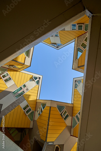 Looking up through a triangular opening in a modern building with yellow and white facades and unusual angles, the sky is clear and blue. Rotterdam, Holland.