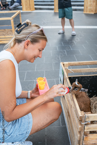 Young woman bottle-feeding a baby goat in an outdoor urban setting