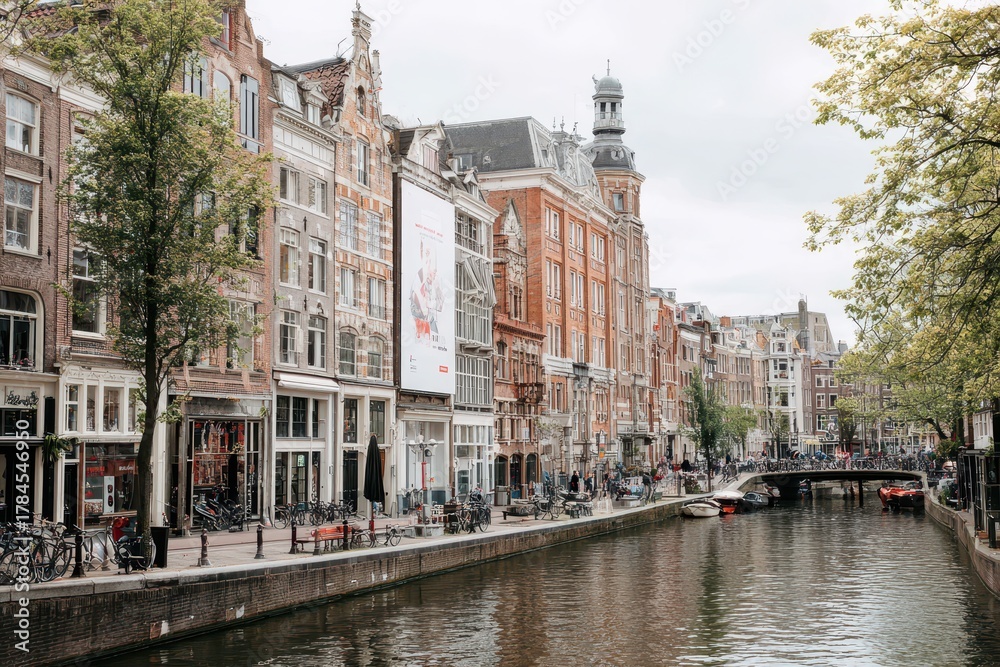 Naklejka premium Urban street Amsterdam near canal, blank billboard on brick building, cobblestones, bicycles moving, pedestrians passing, commercial-ready city mockup photo