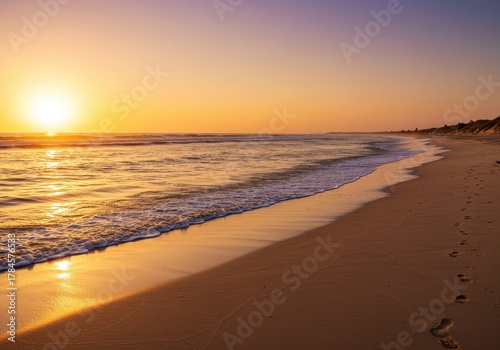 Brilliant sun dips low over tranquil ocean waves washing onto a sandy shoreline.