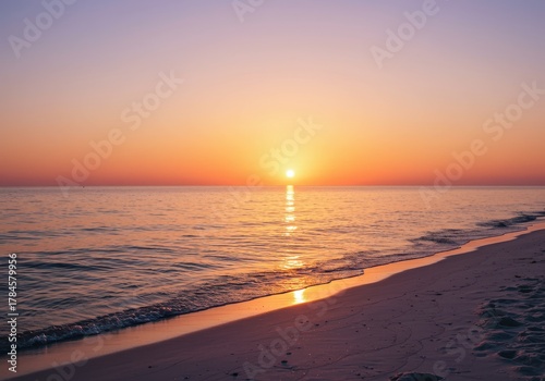Brilliant setting sun reflects intensely across calm ocean water bordering a tranquil sandy shore