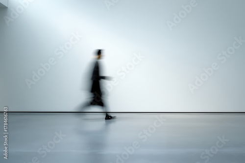 Blurred figure of a man in motion walking rapidly past a white wall in a minimalist interior, concept for speed and efficiency, deadlines and business rush and modern urgency