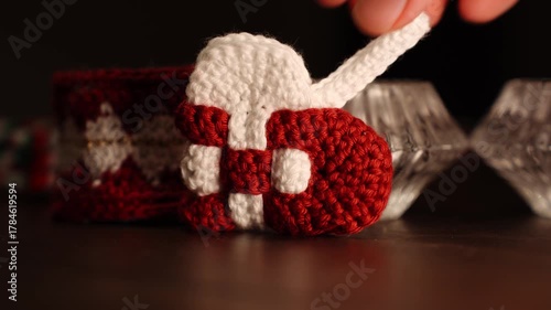 Knitted Christmas heart decoration paced on wooden table, being placed in the frame by a hand.