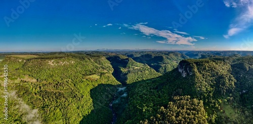 Φωτογραφία Aerial view of lush green canyon and cliffs under blue sky