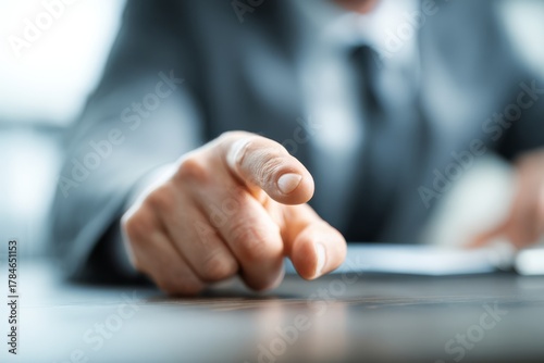 A businessman taps his finger on the desk impatiently, showing curiosity or mild frustration while waiting for answers.