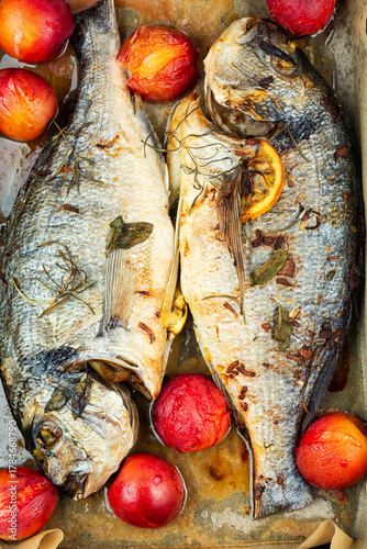 Grilled dorado fish with plums in baking sheet.