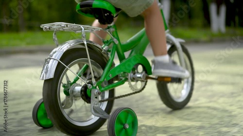 Three year old boy rear view riding green kids bicycle on path in park