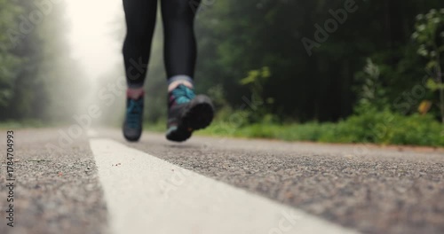Tourist woman young athletic girl  jogging or running on foggy mountain road  next to forest with hiking boots and sport equipment
