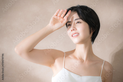 Woman shielding her eyes from the sun's glare against a pink-beige background Close-up evoking UV rays, sun, and sunscreen imagery