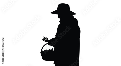 Silhouette of a person in a hat gathering fruit into a basket