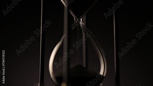 dark sand flowing through a transparent hourglass, symbolizing the quiet passage of time