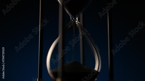 macro cinematic shot of black sand running smoothly in an hourglass, symbol of time, patience, and inevitable change.