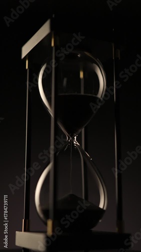 vertical video of black sand hourglass rotating gracefully on a dark background 