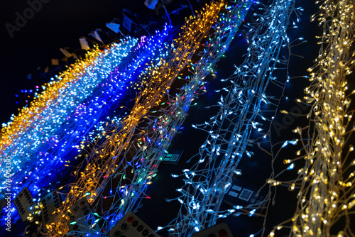 Colorful string lights create a vibrant display at a nighttime festival in a bustling town square during the holiday season