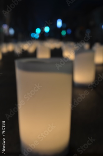 Close-up of a frosted glass votive candle holder with a soft glow in a dark room with blurred background lights.