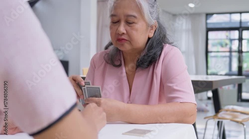 Senior Card Game:  Capturing the essence of quality time, a gray-haired woman intently plays a card game with an unseen opponent.