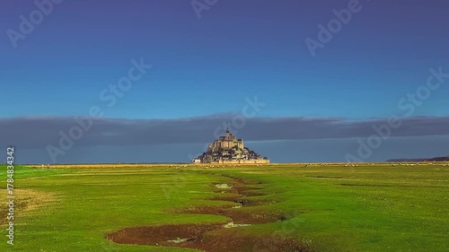 A flock of sheep grazes in a meadow opposite the island fortress Mont Saint-Michel abbey on the coast of Normandy, France. High quality 4k footage