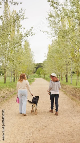Adult women and dog walking together on a dirt road lined with trees