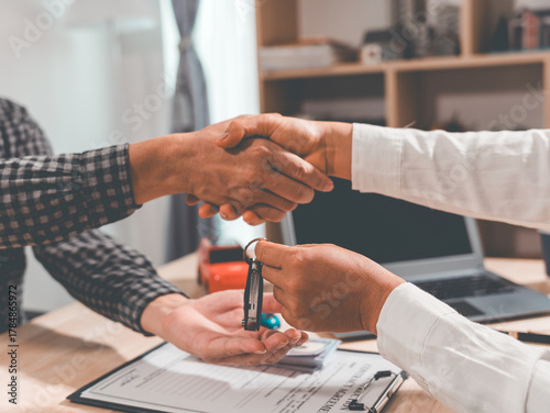Two businessmen agree to buy a used car. They make a contract and stand shaking hands. Salesman and customer are negotiating in sales office. Concept of buying or selling a car.