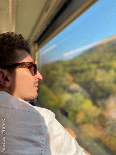 a man sitting on a train looks at the landscape from the window.