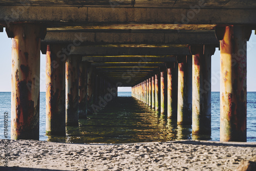 Fototapeta Naklejka Na Ścianę i Meble -  Rusted pier pillars extending over Baltic Sea shoreline at sunset