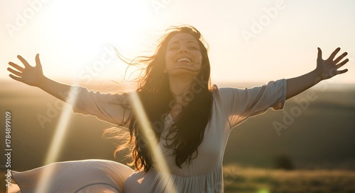 Happy young woman with long hair smiling freely with her arms outstretched in a sunny field at sunset, embracing the warm light and feeling pure joy