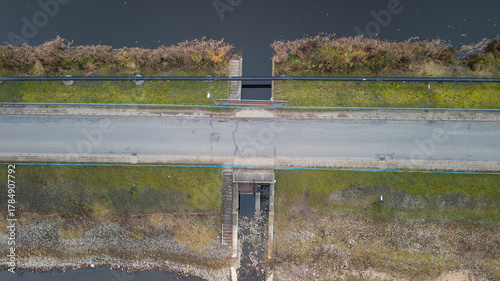 An aerial view captures a serene waterway bisected by a road and parallel pipeline on a quiet day.