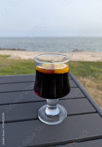 Close-up of a drinking glass on a table with a cola and lemon slices in the garden overlooking the sea.