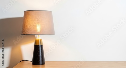 A table lamp with a beige lampshade and a black base, casting a warm glow on a wooden table.