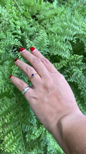 4k video footage of The fingers of a beautiful woman with red nail polish, adorned with gold and silver rings set with diamonds and blue sapphires with green lush leaves and plants background