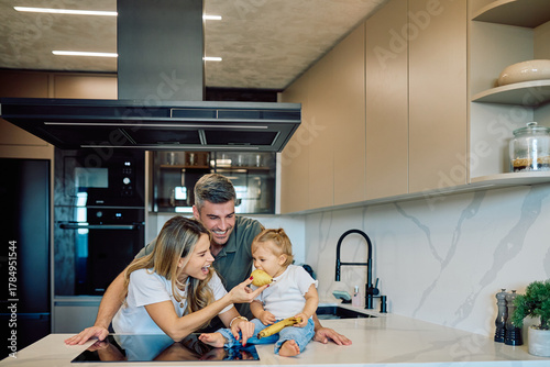 Obraz na płótnie Happy family bonding, parents giving their baby fruit on a kitchen island, enjoy