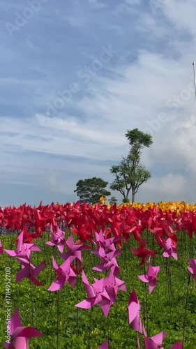 4k video footage of Colorful plastic toy pinwheels spinning fast in the wind at an open public park with trees and cloudy sky background.
