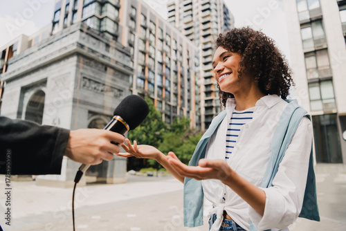 Valokuva Smiling woman in striped shirt being interviewed on an urban street with microph