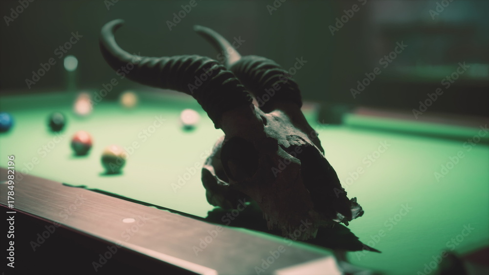 Obraz premium In a dimly lit room, a goat skull rests on the edge of a vibrant green pool table surrounded by colorful billiard balls. The eerie ambiance adds a touch of mystery to the scene.