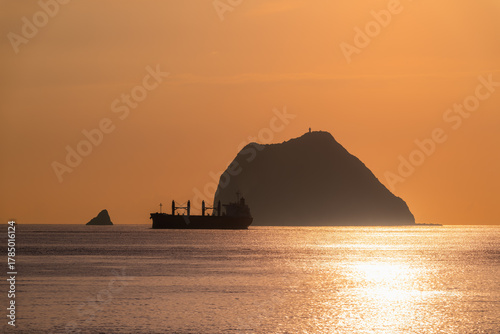 See the silhouette of a cargo ship sailing near Keelung Islets at Waishuangxi, Taiwan. Filmed on June 23, 2025, during a calm summer morning.