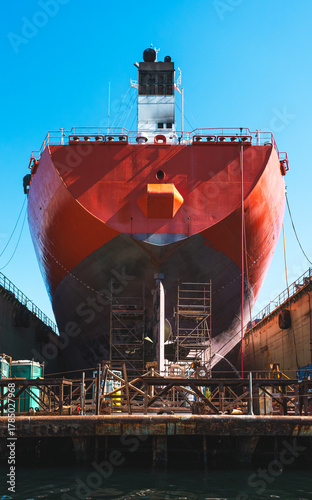 Massive cargo ship under maintenance in dry dock with scaffolding and bright blue sky, industrial maritime scene, shipyard engineering concept.